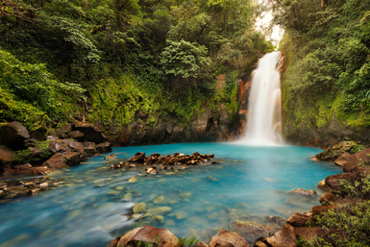 Wasserfall mündet in einem blauschimmernden See, umgeben von grünem dichten Wald